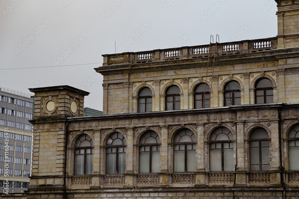 Obraz premium Historic Building Facade Featuring Arches Windows and a Ladder on a Cloudy Day in an Urban Setting