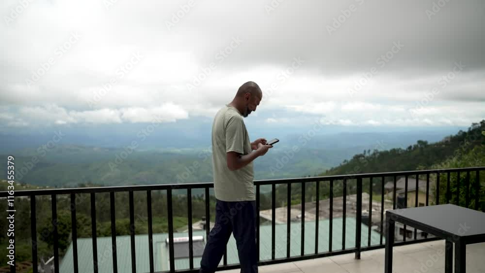 Man standing on a scenic balcony checking his phone with mountains in view. Man standing on a scenic balcony checking his phone with mountains in view.