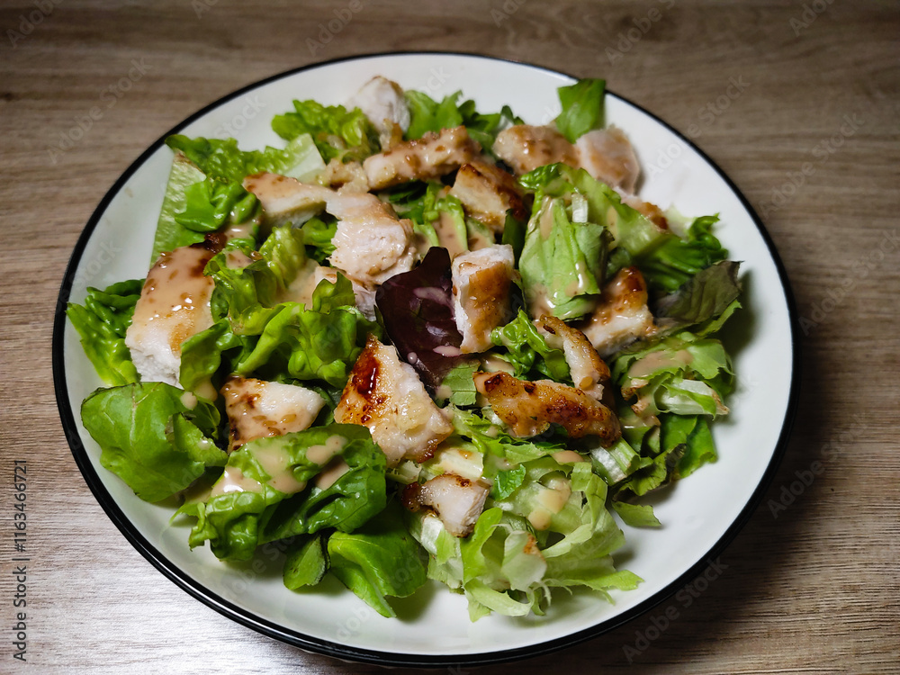 A plate of fresh Caesar salad with grilled chicken, lettuce, and creamy dressing. A plate of fresh Caesar salad with grilled chicken, lettuce, and creamy dressing.