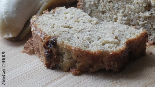 Left pan view of banana bread cut in half on a wooden board with a bananas in the back. photo