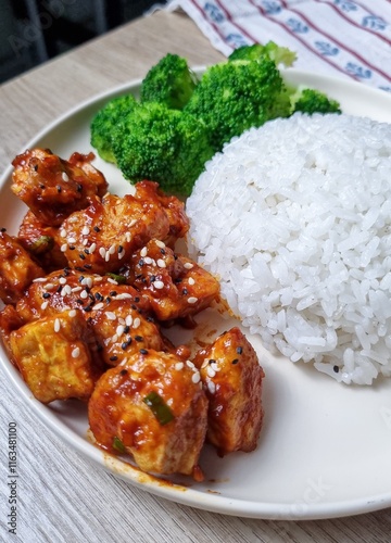 A plate of Korean-style tofu with sesame seeds, served with steamed rice and broccoli.
