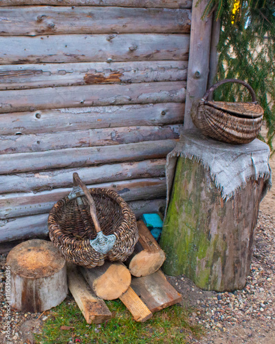 A stump with wicker baskets and chopped wood near a rustic log wall.