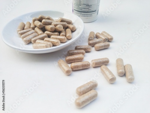 High angle view of capsule pills in a small white plate and bottle on a white background.  photo