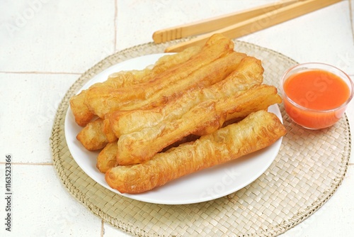 Golden and crispy youtiao, also known as cakwe or Chinese fried dough sticks,served on a white plate. Perfectly fried to perfection,these savory treats are ideal for breakfast or pairing with porridge photo