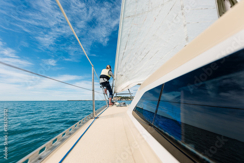 Teenager sitting on rail of sailboat on beautiful day photo