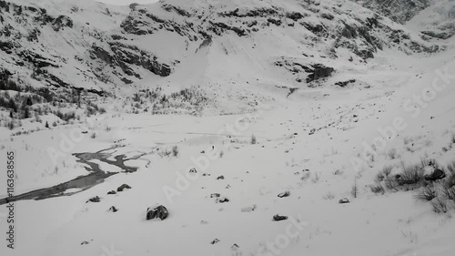 Aerial footage of a skier exploring a remote alpine valley within the Swiss Alps in Valais, Switzerland with a view of the snow covered mountains peaks, glaciers and cliffs on a cloudy winter day photo