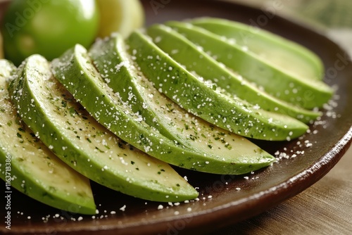 Freshly sliced green avocados sprinkled with seasoning, served on a rustic plate.