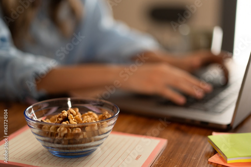 Bowl of walnuts on a desk with a person typing on a laptop - Mindful eating habits with healthy snacks while working