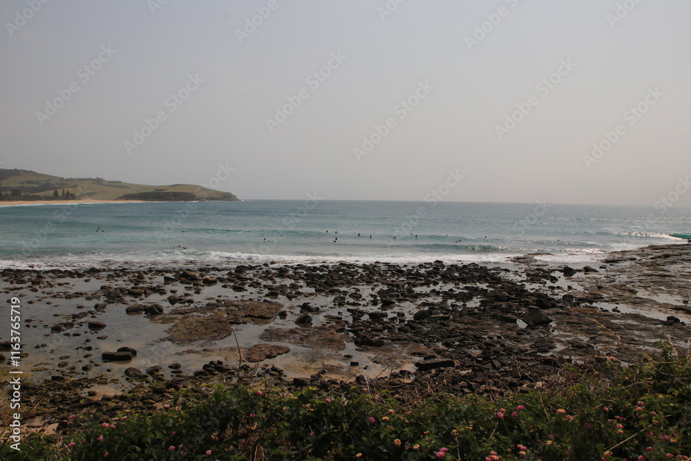 A serene coastal view showcasing a rocky shoreline with gentle ocean waves rolling in under a soft, hazy sky. Distant landforms add depth to the scene, creating a tranquil ambiance A serene coastal view showcasing a rocky shoreline with gentle ocean waves rolling in under a soft, hazy sky. Distant landforms add depth to the scene, creating a tranquil ambiance
