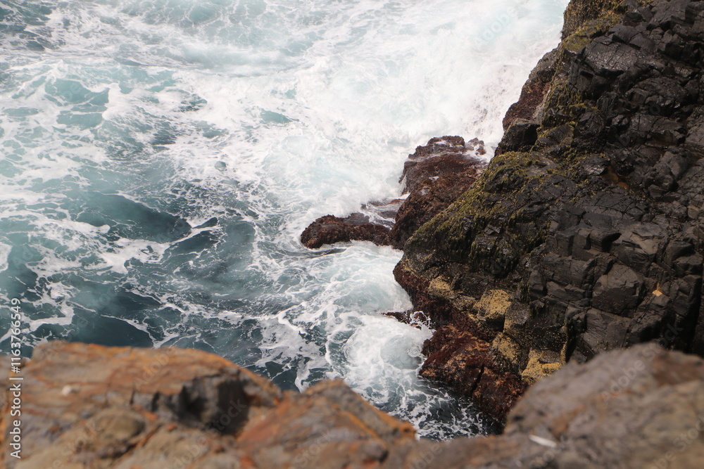 A dramatic close-up of ocean waves crashing against rugged, jagged rocks, highlighting the raw power and untamed beauty of nature's force at the water's edge A dramatic close-up of ocean waves crashing against rugged, jagged rocks, highlighting the raw power and untamed beauty of nature's force at the water's edge