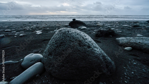 Black rocks on the black sand beach of Vík, Iceland, with ocean waves and sky captured in an ultra-wide-angle focus composite.