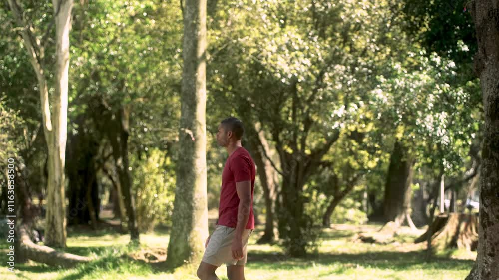 Focused African American man walking calmly through a park on a sunny day. Side view tracking shot of the athlete in casual clothes, enjoying a peaceful stroll among nature Focused African American man walking calmly through a park on a sunny day. Side view tracking shot of the athlete in casual clothes, enjoying a peaceful stroll among nature