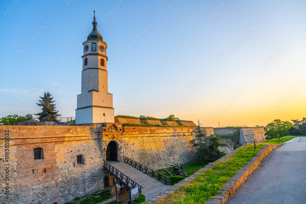 Fototapeta premium As the sun sets over Belgrade, the Clock Tower and Clock Gate at Kalemegdan Fortress illuminate the historic site, highlighting its ancient architecture and serene surroundings.