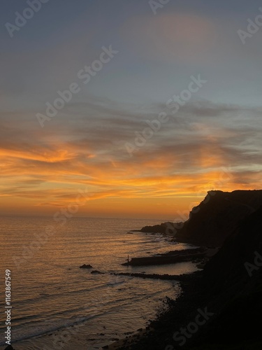 a sunset lightens up the sky with orange clouds which disappear behind the dark clif photo