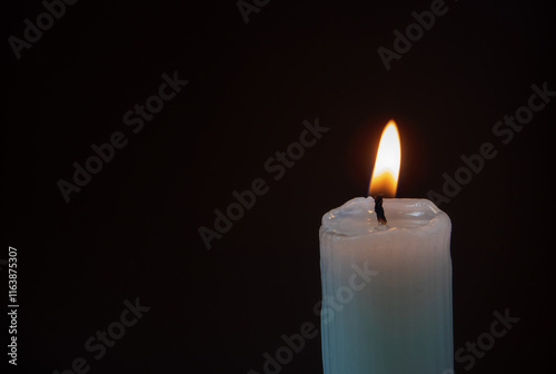 Burning ribbed pillar wax candle on the dark background photo