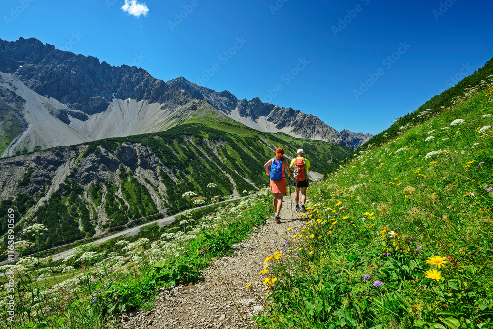 Man and woman hiking on Hahntennjoch mpuntain pass amidst meadow under blue sky Man and woman hiking on Hahntennjoch mpuntain pass amidst meadow under blue sky