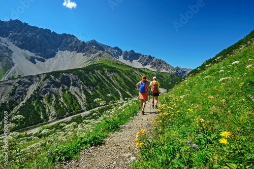 Man and woman hiking on Hahntennjoch mpuntain pass amidst meadow under blue sky photo