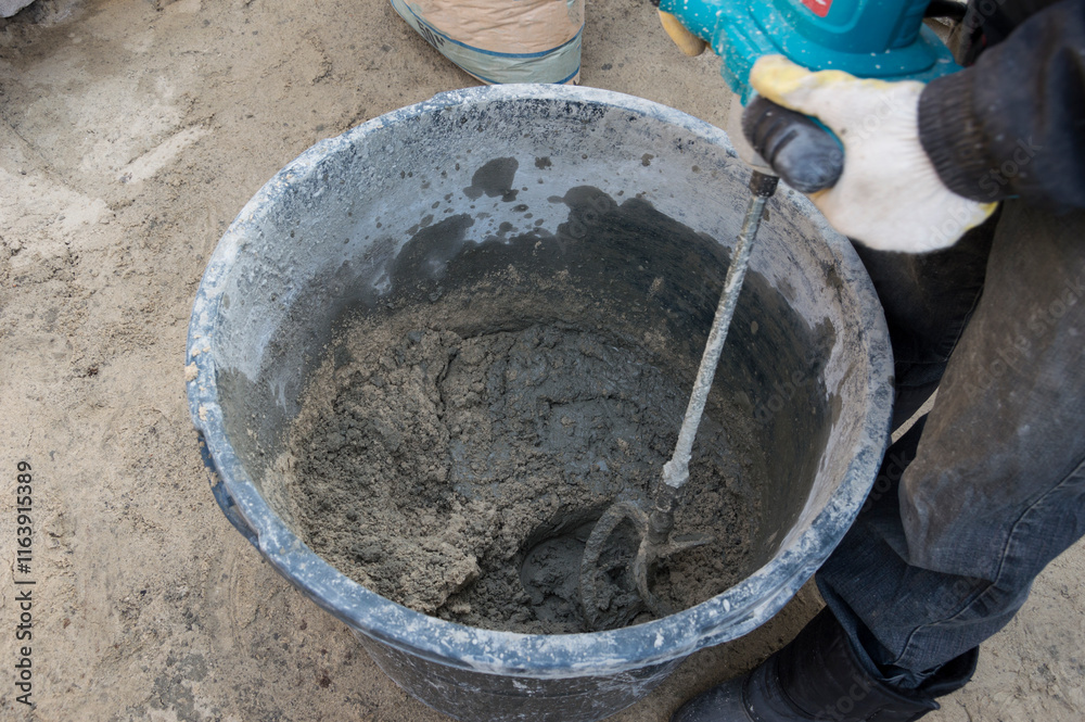 Mixing concrete in a bucket using a handheld concrete mixer. Mixing concrete in a bucket using a handheld concrete mixer.