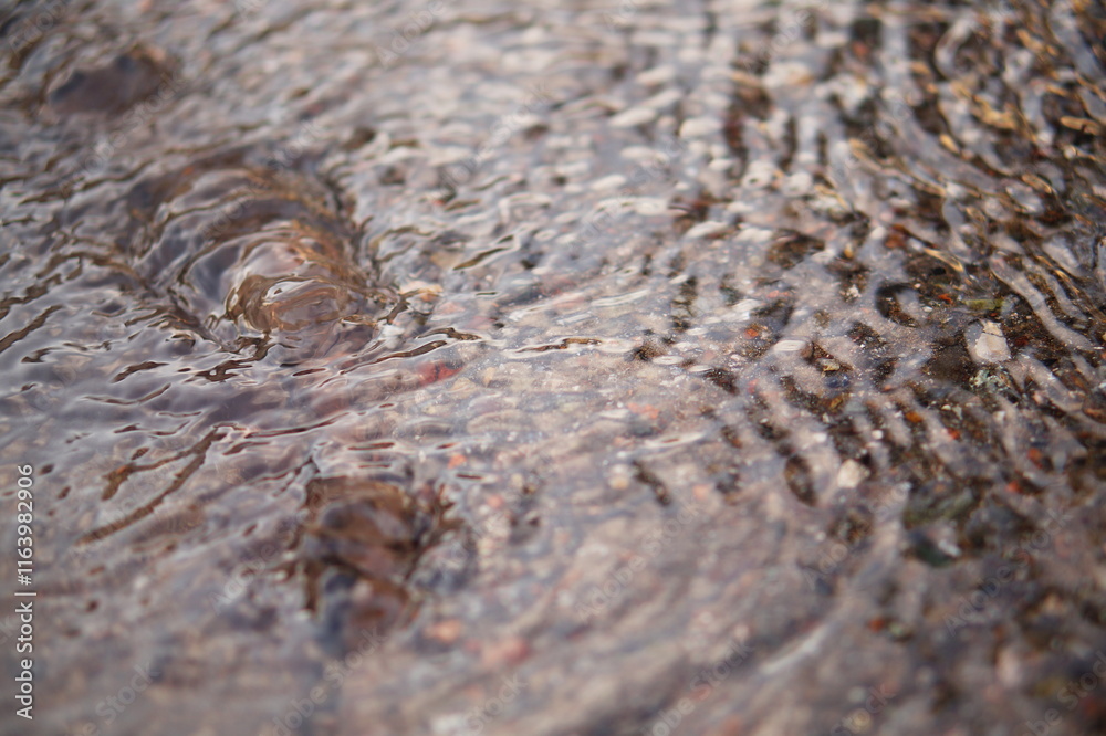 The camera captures a shallow stream of water flowing down the surface of the asphalt, forming small waves. Then it comes to a spring that bursts out of the ground, rising to the surface The camera captures a shallow stream of water flowing down the surface of the asphalt, forming small waves. Then it comes to a spring that bursts out of the ground, rising to the surface