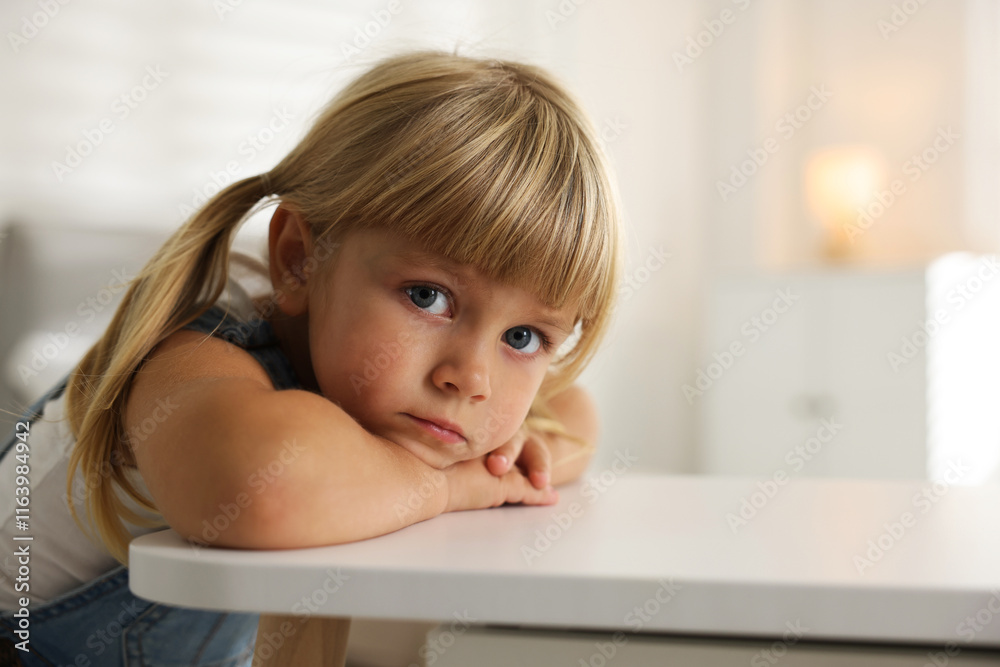 Orphanage concept. Sad little girl at table indoors, space for text Orphanage concept. Sad little girl at table indoors, space for text