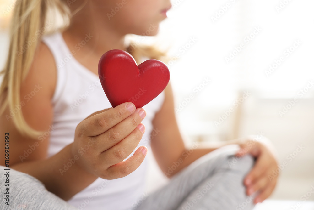 Orphanage concept. Little girl with red heart figure indoors, closeup. Space for text