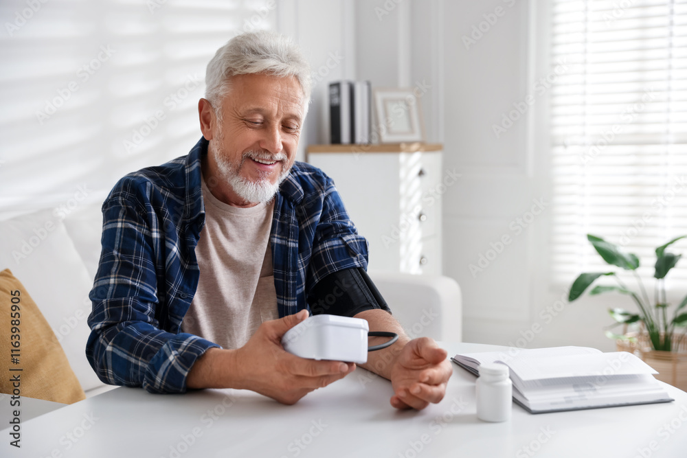 Senior man measuring blood pressure at table indoors Senior man measuring blood pressure at table indoors