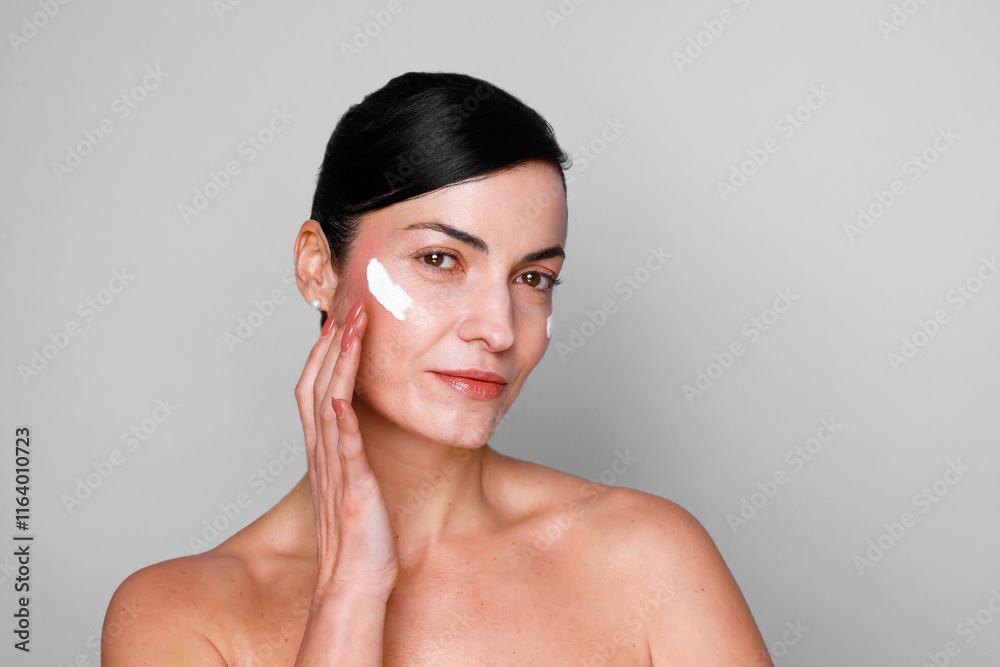 Beautiful mature woman looking at camera and applying moisturizing skincare cream, lotion or mask for skin lifting and anti-aging detoxifying effect, white background Beautiful mature woman looking at camera and applying moisturizing skincare cream, lotion or mask for skin lifting and anti-aging detoxifying effect, white background