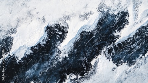 Aerial view of dramatic snow covered glacial ridges and dark ocean waves illustrating the contrast of nature's beauty and power