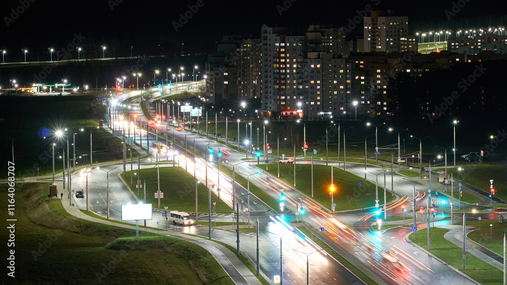 Obraz premium Car traffic in the night city. Traces of light from the headlights on the street. Top view of the roadway near residential buildings. Slow motion, soft focus.