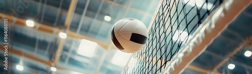White leather volleyball seen from below, soaring over the net during a match in an indoor arena  -