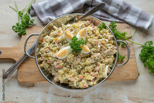 Delicious russian winter salad olivier with potatoes, green peas, sausage, pickles, carrots, mayonnaise and onions in a bowl photo