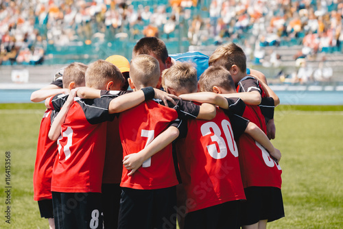 Fototapeta Naklejka Na Ścianę i Meble -  Teenage boys in a sports team. Sports team friendship. Group of sports players with coach huddling in a circle and motivating each other. Boys in red jersey shirts with numbers