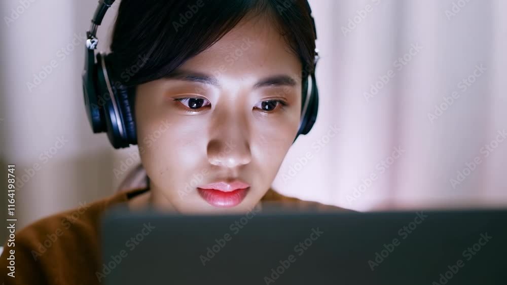 Asian young woman with headphones in front of laptop at home. Online education. A young woman studies diligently from home, earphones blocking distractions for better focus. Asian young woman with headphones in front of laptop at home. Online education. A young woman studies diligently from home, earphones blocking distractions for better focus.