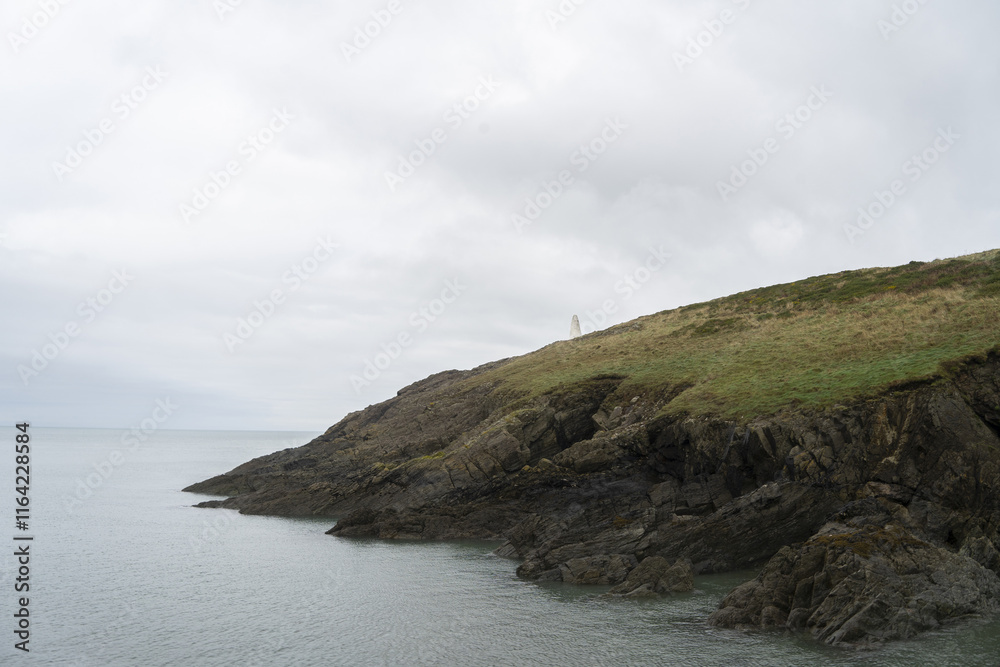 serene coastal landscape with a tranquil cove framed by rugged cliffs. A rocky shore covered in dark pebbles and seaweed leads to calm, reflective waters. Mist and overcast skies enhance the peace serene coastal landscape with a tranquil cove framed by rugged cliffs. A rocky shore covered in dark pebbles and seaweed leads to calm, reflective waters. Mist and overcast skies enhance the peace