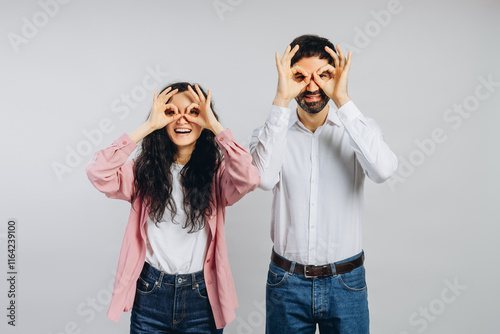 Cheerful couple mimicking glasses with fingers on white background