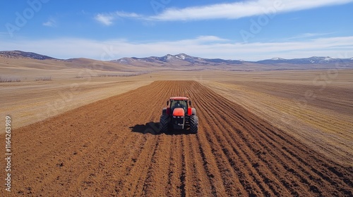 Tractor plowing fields on rural farmland with hills in the background during ...