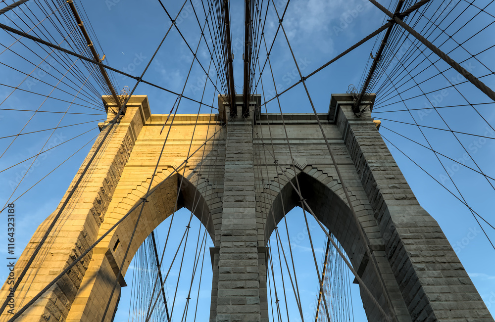 Obraz premium Brooklyn Bridge close up detail looking up at suspension cables at sunrise (beautiful landmark travel tourism destination in NYC) iconic New York City attraction over east river downtown Manhattan USA