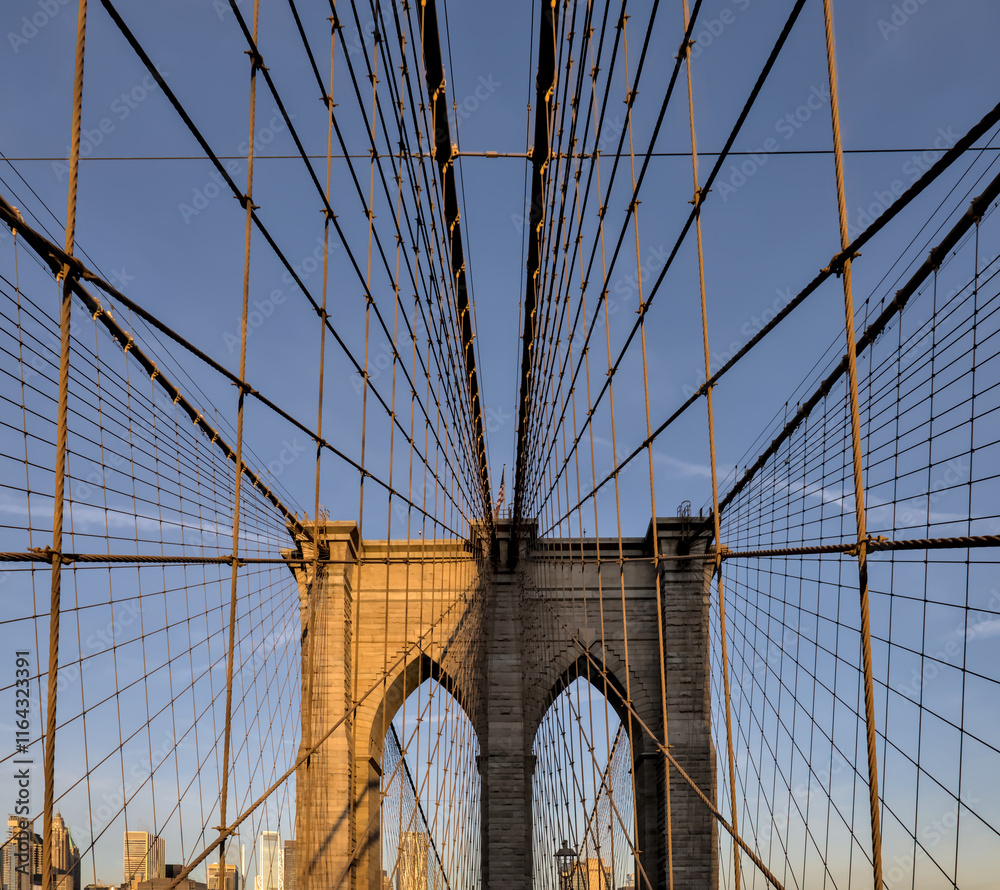 Fototapeta premium Brooklyn Bridge close up detail looking up at suspension cables at sunrise (beautiful landmark travel tourism destination in NYC) iconic New York City attraction over east river downtown Manhattan USA