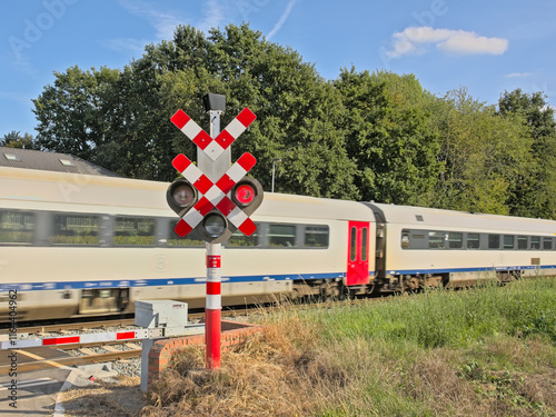 Canvas Print Passenger train with movement blur while passing a level crossing with red signa