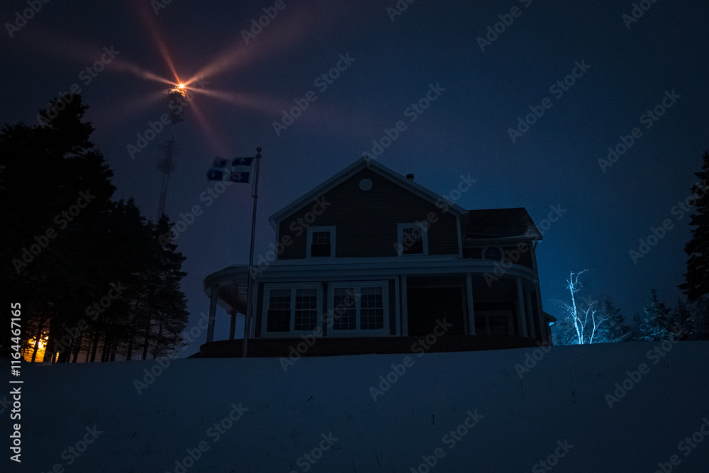 Mountain House Lit Up at Night in Winter Landscape in Anticosti Island, Quebec with Lighthouse Behind