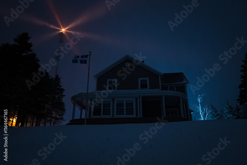 Obraz na płótnie Mountain House Lit Up at Night in Winter Landscape in Anticosti Island, Quebec with Lighthouse Behind w salonie