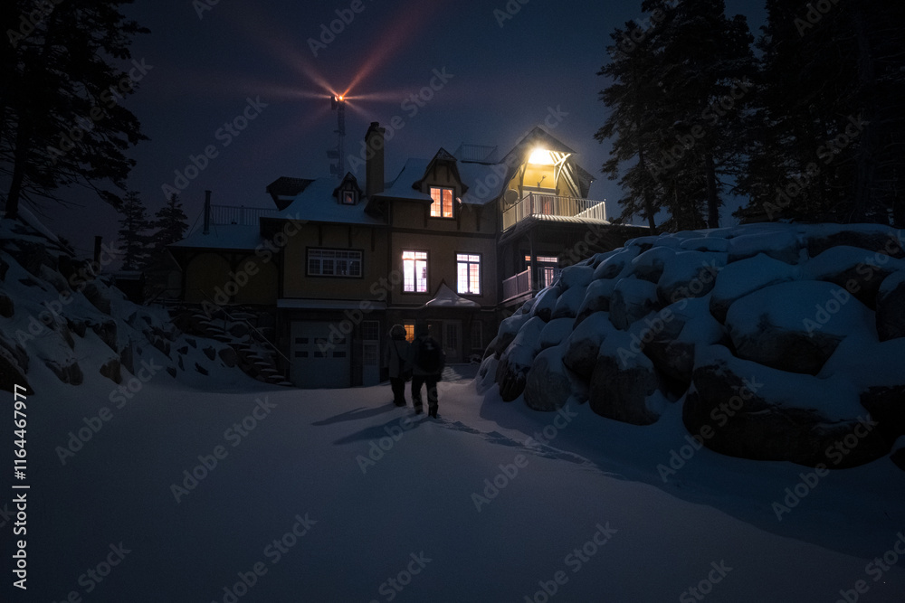 Mountain House Lit Up at Night in Winter Landscape in Anticosti Island, Quebec with Lighthouse Behind