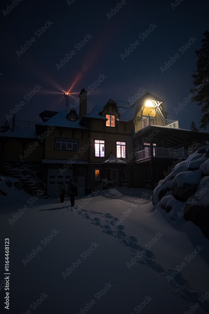 Mountain House Lit Up at Night in Winter Landscape in Anticosti Island, Quebec with Lighthouse Behind