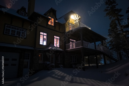 Obraz na płótnie Mountain House Lit Up at Night in Winter Landscape in Anticosti Island, Quebec with Lighthouse Behind w salonie