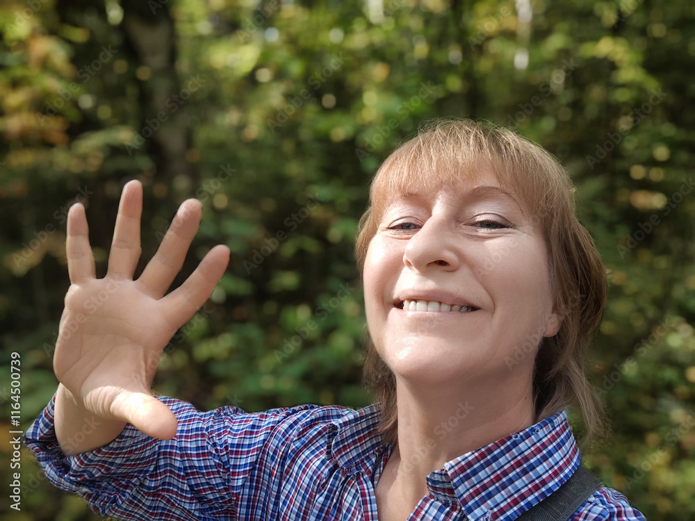 Middle-aged woman shares travel experience through a cheerful selfie in a lush green forest Middle-aged woman shares travel experience through a cheerful selfie in a lush green forest