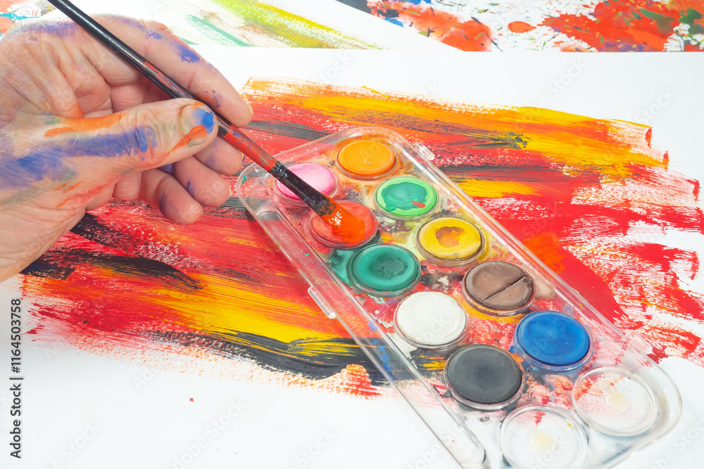 Obraz premium The photo shows the artist's hands with a brush against a background of watercolor paints.