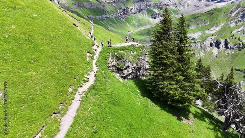 Slow back drone flight above some hikers on a mountain trail high above the Oeschinensee lake in the  Swiss Alps. Beautiful Swiss mountains with hiking trail, some hikers enjoying nature. Outdoor adve