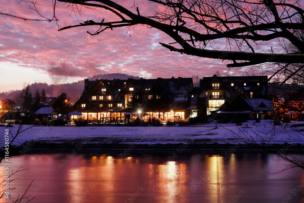 SROMOWCE NIZNE, POLAND - DECEMBER 28, 2024: Beautifully illuminated hotel and restaurant seen at sunset from the opposite bank of the river.