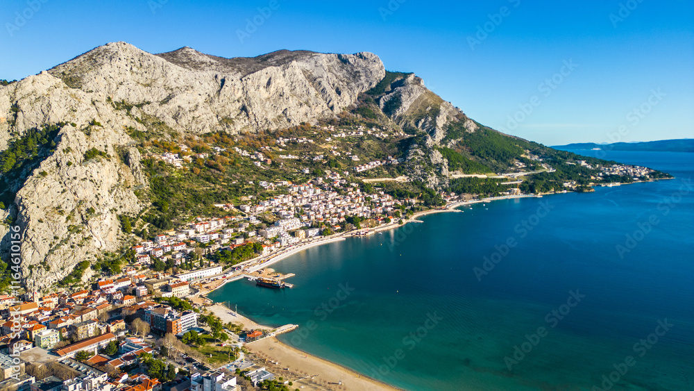 Obraz premium An aerial shot of Omiš(Omis), Croatia, captured from a drone, revealing the town’s stunning historic castle perched on a hilltop overlooking the Adriatic Sea. The famous Omis Bridge