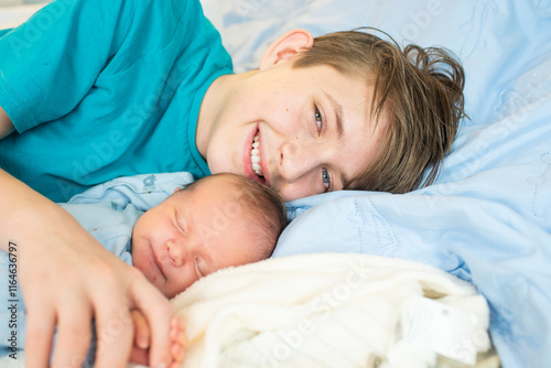 12 year old boy hugs his sleeping newborn brother. Happy teenager lies with his baby brother on the bed. photo